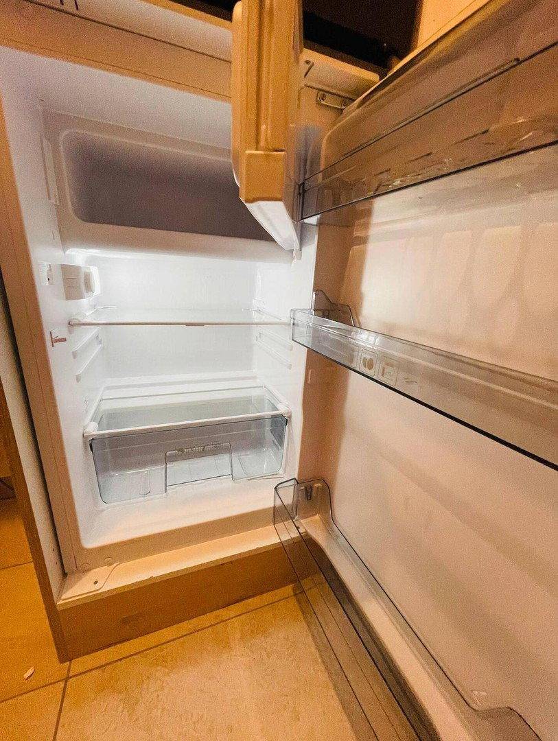 Offener Kühlschrank mit leeren Regalböden und Gefrierfach in einer Küche.