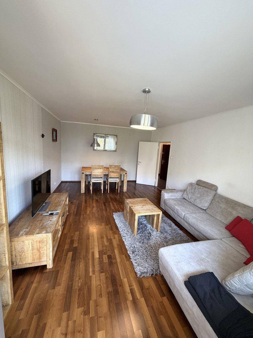Geräumiges Wohnzimmer mit bequemer Couch und Essbereich im Hintergrund, heller Holzboden.