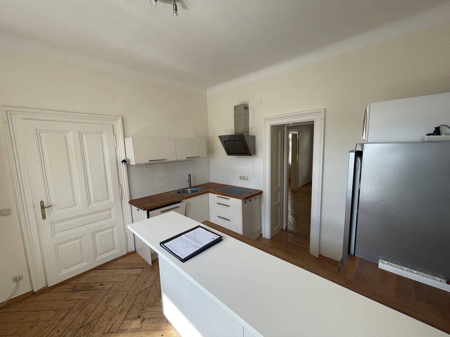 Funktionale Küche mit weißen Unterschränken, Holzarbeitsplatte und einem Kühlschrank.