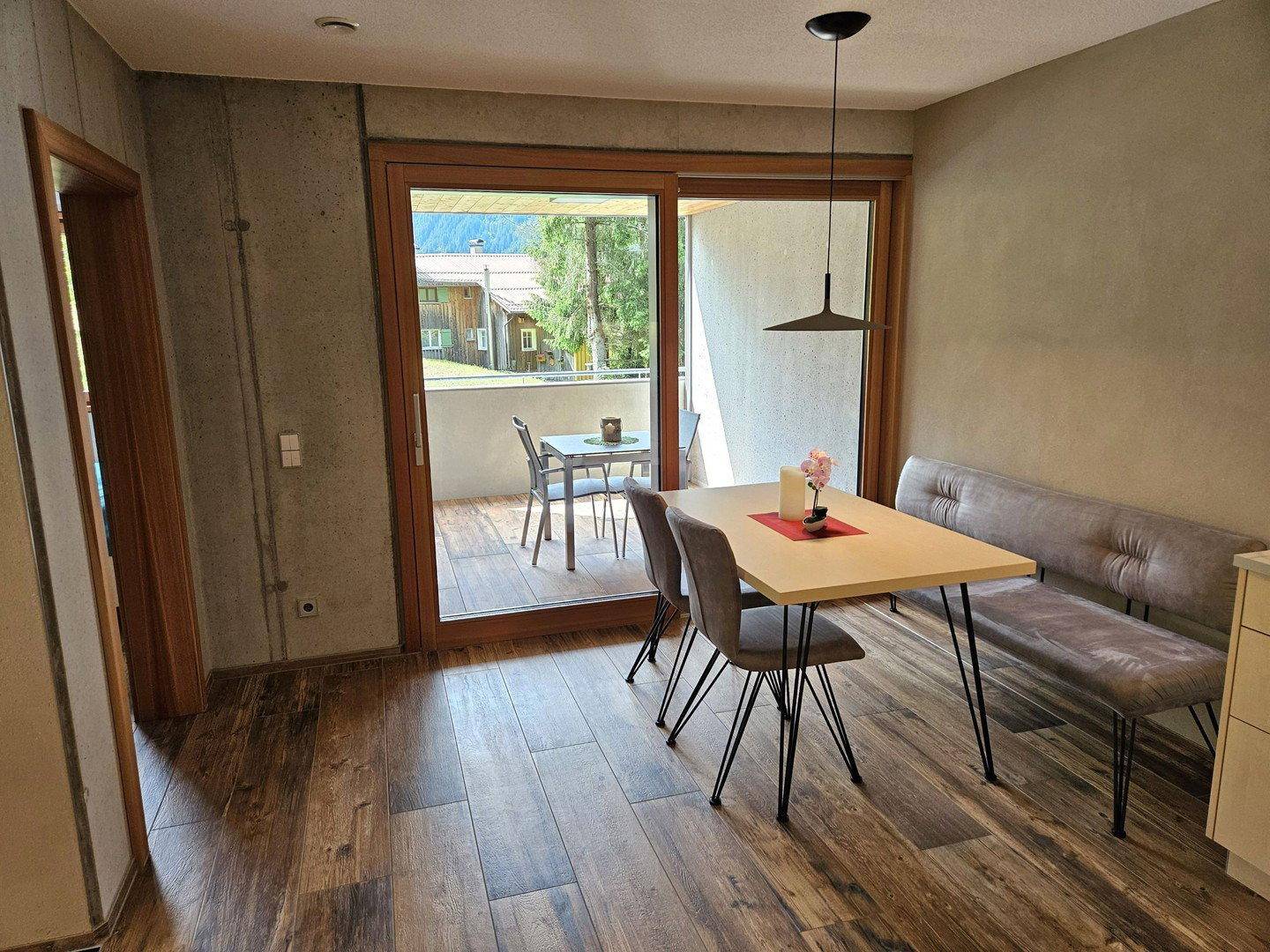 Essbereich mit Holzboden und modernem Tisch, direktem Zugang zum Balkon und Blick ins Grüne.