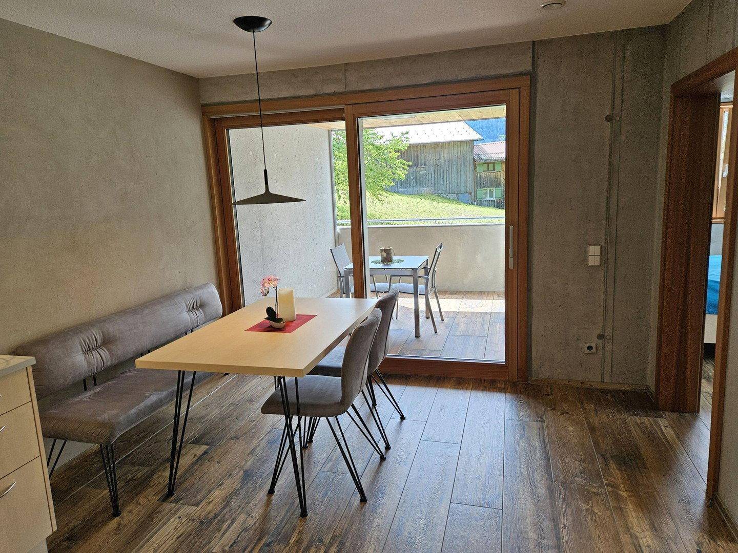 Essbereich mit Holzboden und modernem Tisch, direktem Zugang zum Balkon und Blick ins Grüne.