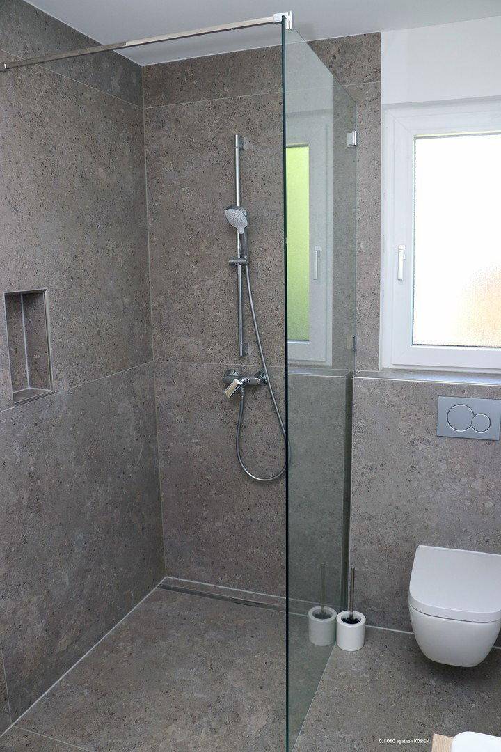 Modernes Badezimmer mit ebenerdiger Dusche, grauen Fliesen und wandhängendem WC.