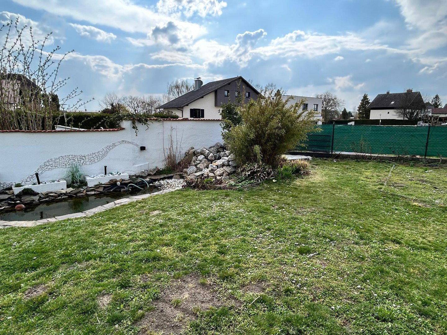 Weitläufiger Garten mit grünem Rasen, dekorativem Teich und umgebender Bepflanzung.