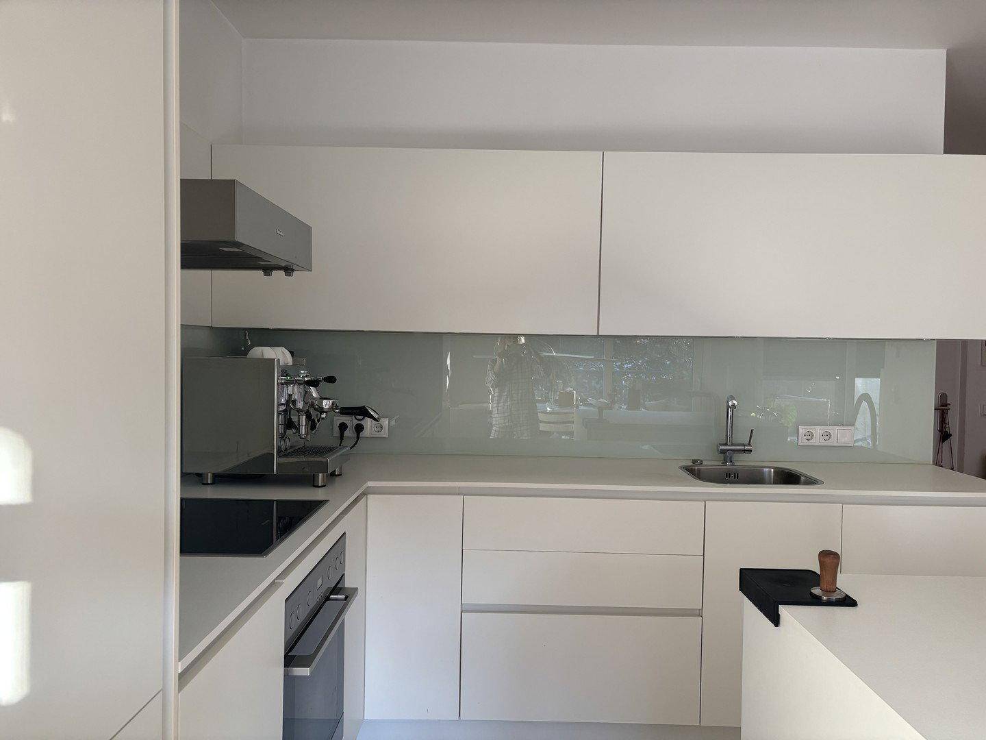 Moderne weiße Küche mit Hochglanzfronten, integrierten Geräten und Kaffeemaschine.