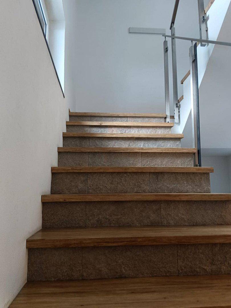 Treppenaufgang mit Holzstufen und Fliesenakzenten, modernem Geländer und weiß gestrichenen Wänden.