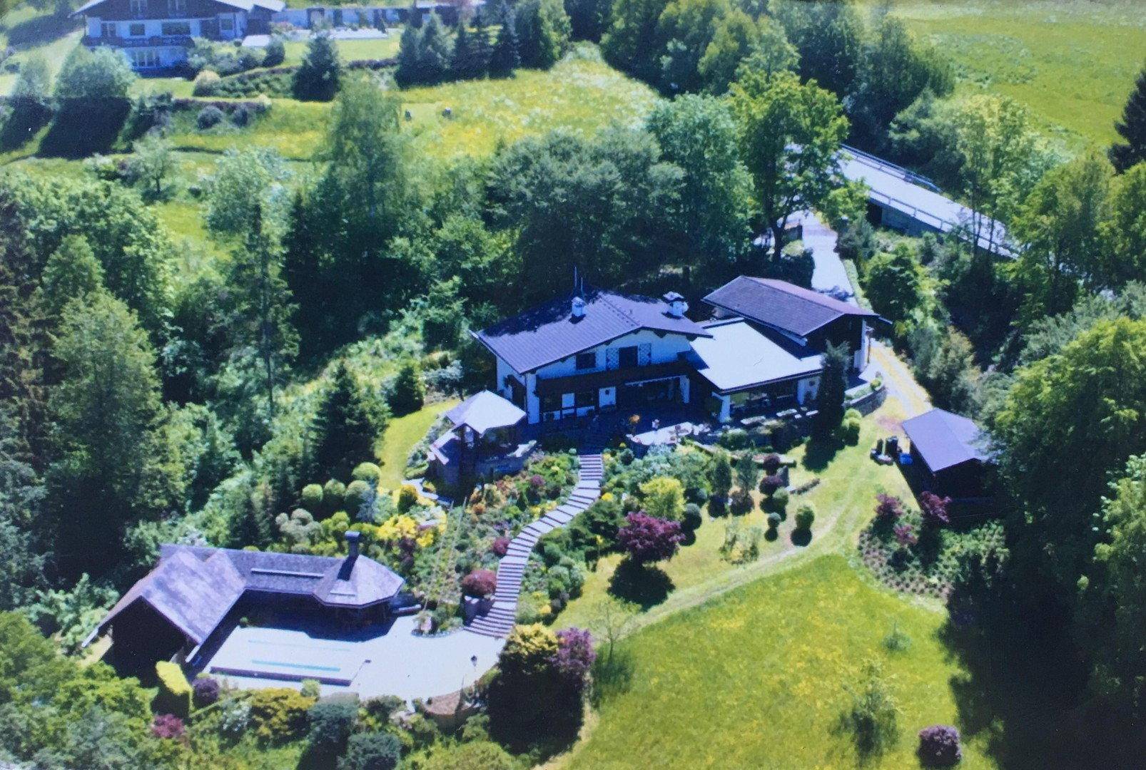 Luftaufnahme eines weitläufigen Anwesens mit Haupthaus, Nebengebäuden und großzügiger Gartenanlage.