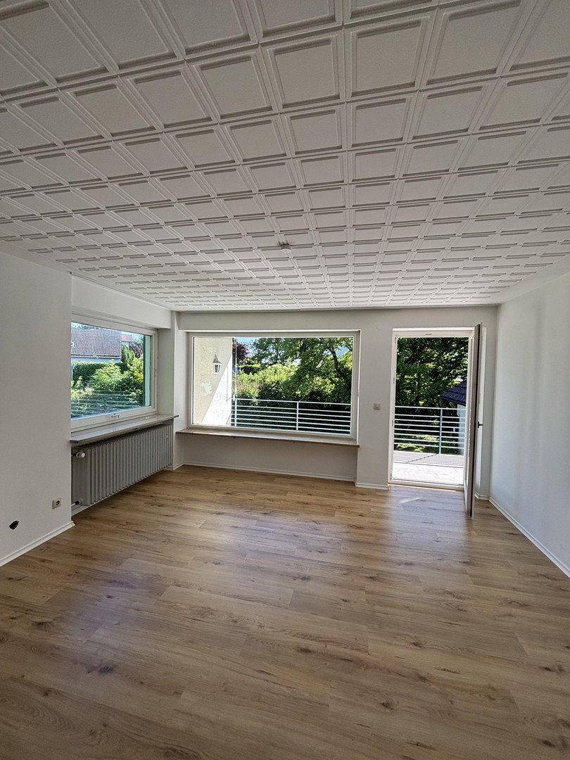 Helles Zimmer mit Holzboden, Kassettendecke und Zugang zu einem Balkon.