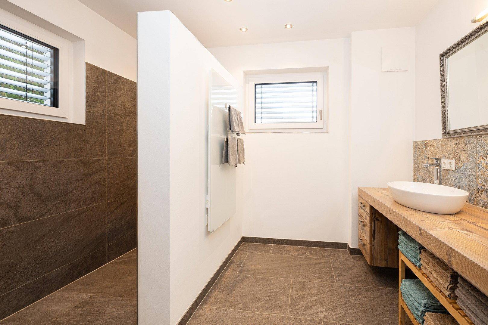 Modernes Badezimmer mit begehbarer Dusche, Holzwaschtisch und zwei Fenstern.