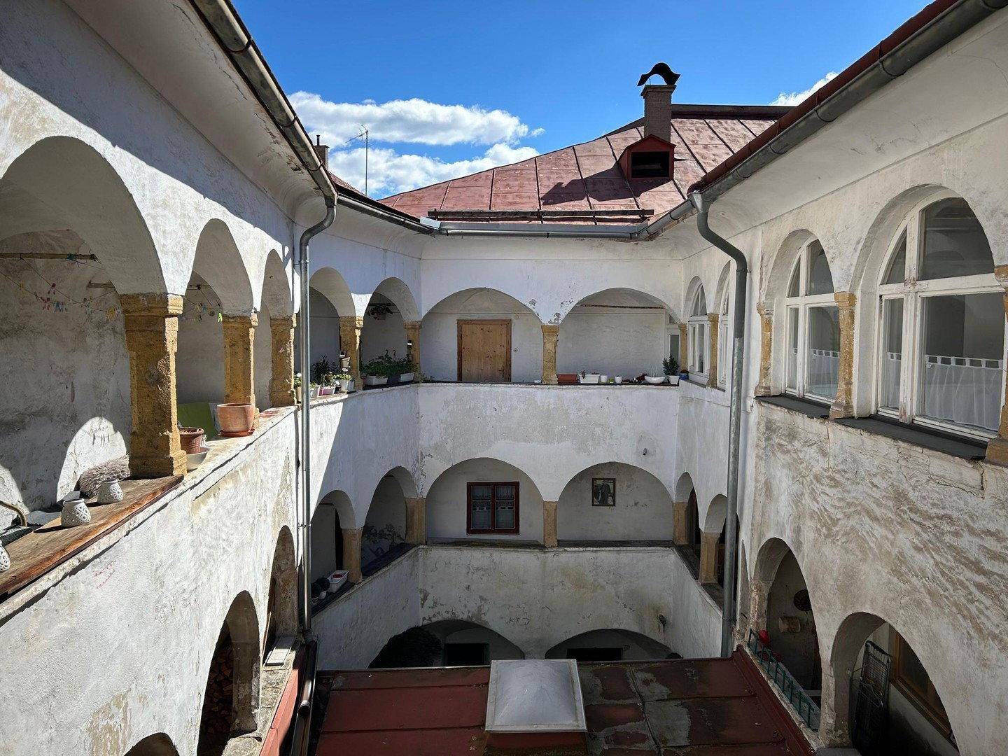 Historischer Innenhof mit Arkaden, mehreren Etagen und traditioneller Architektur unter blauem Himmel.