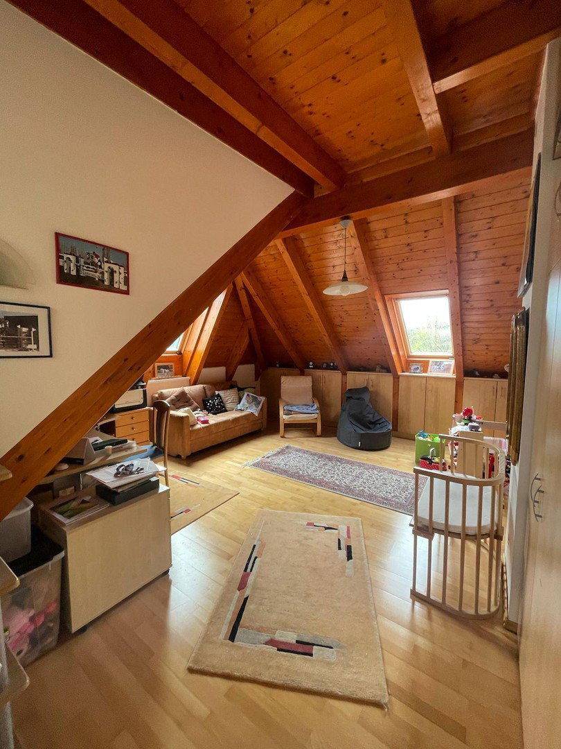 Heller Dachbodenraum mit Holzbalken, Dachfenstern und gemütlicher Sitzecke unter schräger Decke.