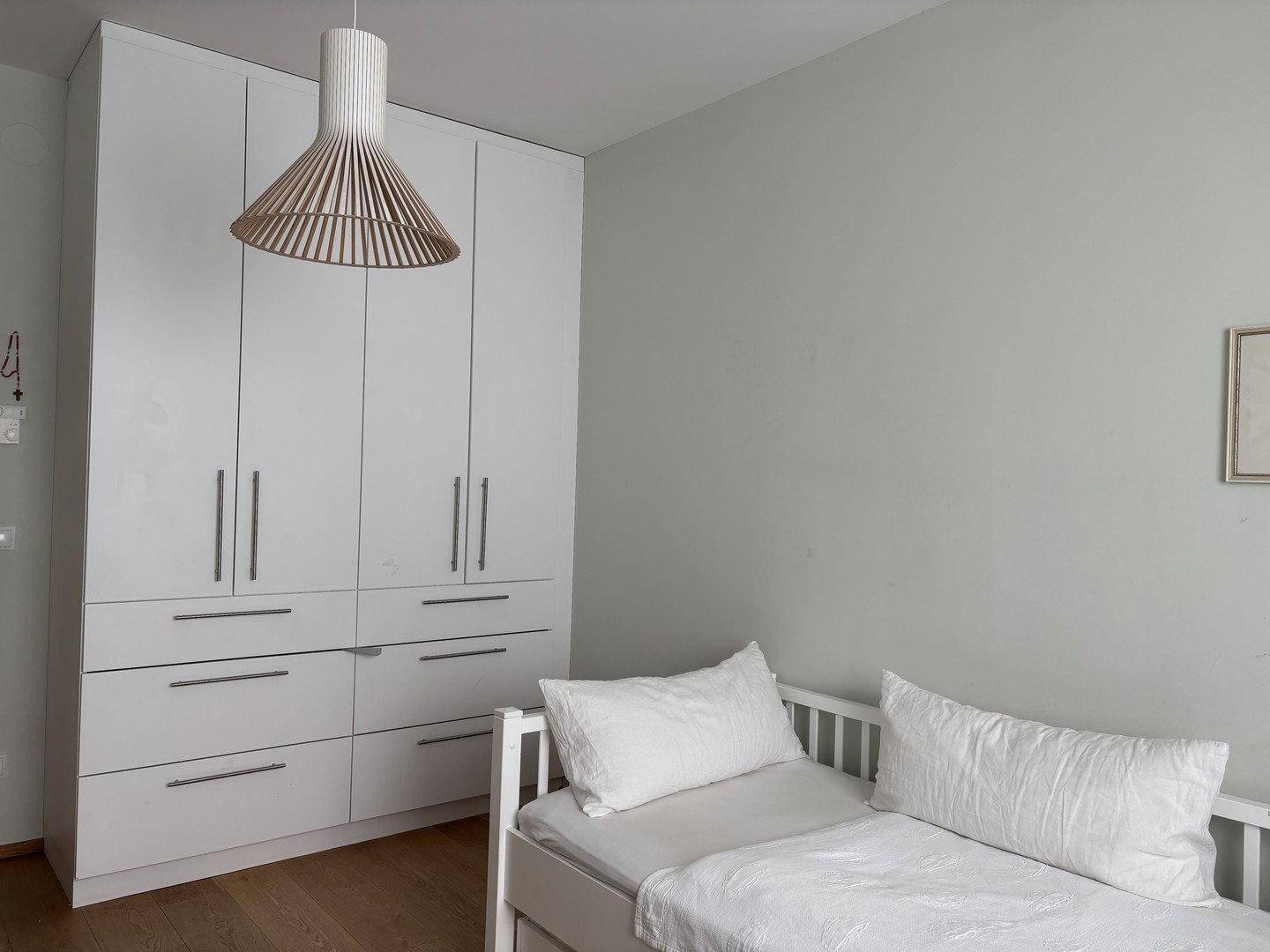 Schlafzimmer mit weißem Einbauschrank, Einzelbett und hellem Holzboden.