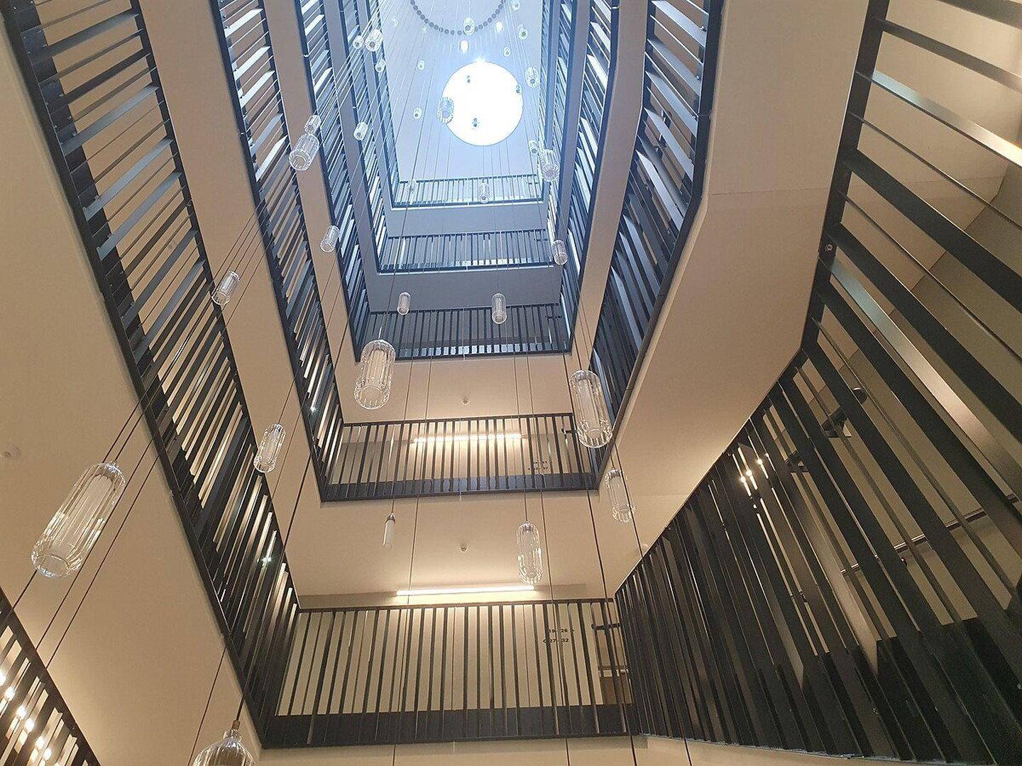 Modernes Treppenhaus mit mehreren Etagen, Metallgeländern und dekorativen Hängelampen.