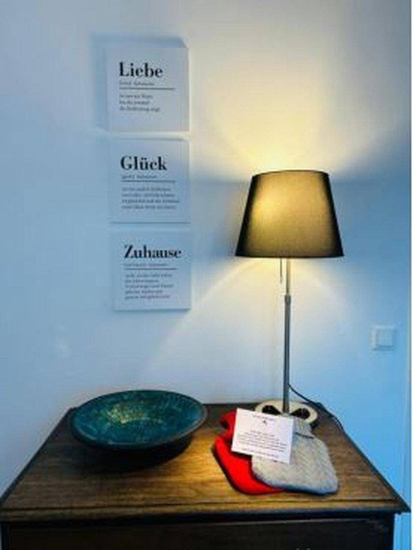 Dekorative Wandbilder mit deutschen Wörtern "Liebe", "Glück", "Zuhause" neben einer Tischlampe.