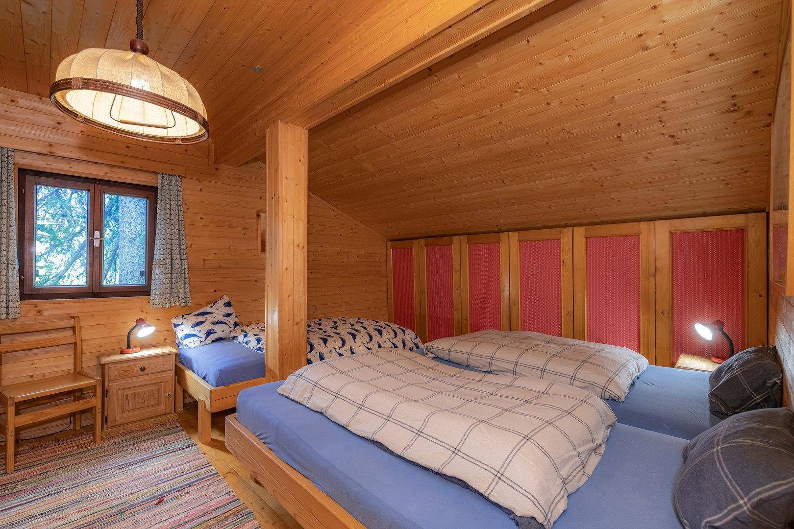 Schlafzimmer mit schräger Holzdecke, mehreren Betten und eingebauten Kleiderschränken.