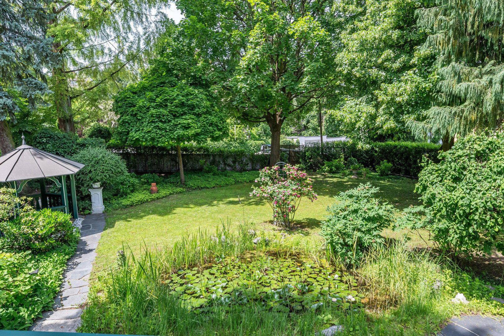 Gepflegter Garten mit Teich, üppiger Vegetation und einem kleinen Pavillon.