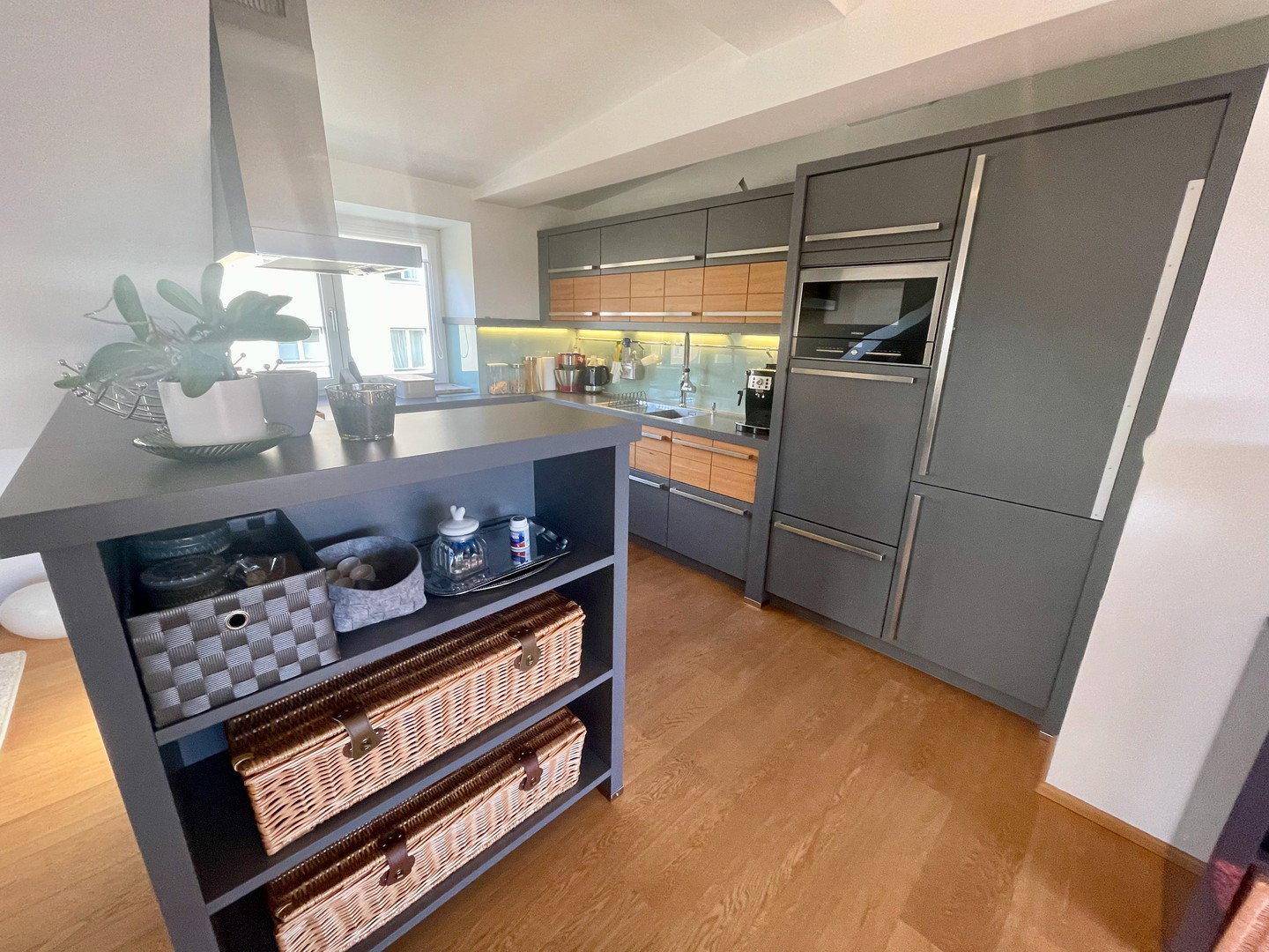 Moderne Küche mit grauen Schränken, Holzelementen und einer praktischen Kücheninsel mit Stauraum.