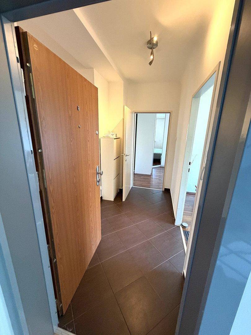 Eingangsbereich mit offener Holztür und dunklen Fliesen, führt in die Wohnung.