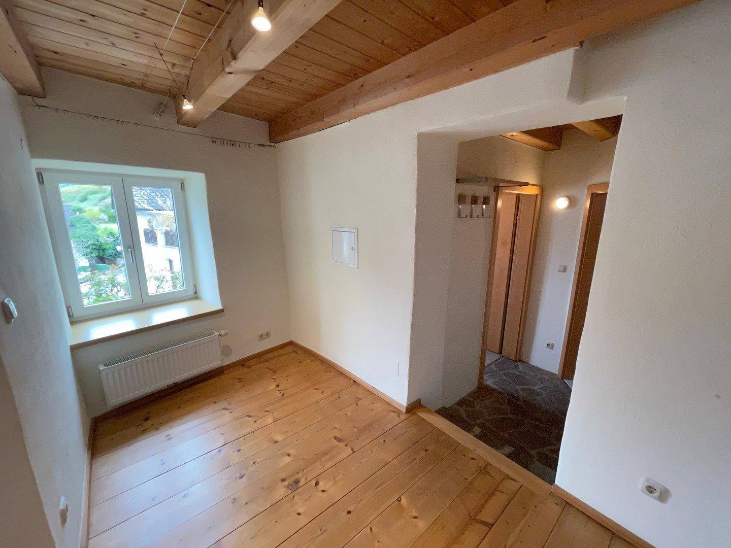 Gemütlicher Raum mit Holzdielenboden, sichtbaren Deckenbalken und einem Fenster mit Blick ins Grüne.