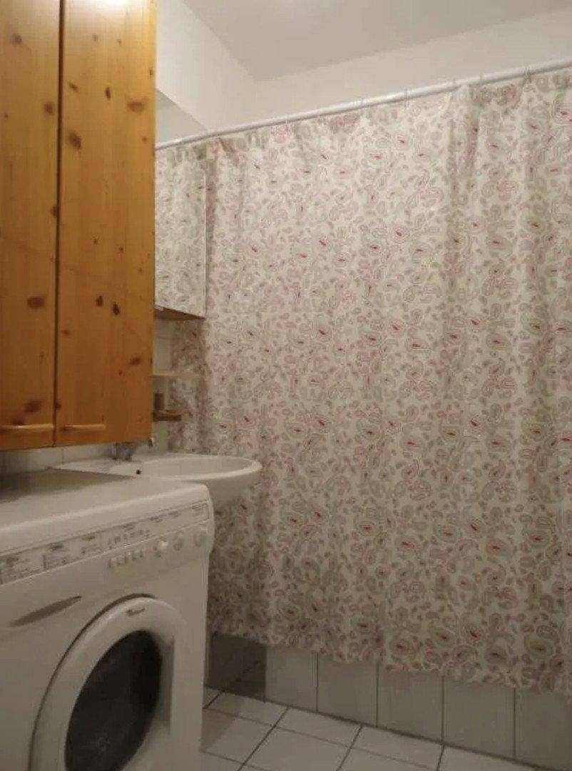 Badezimmer mit Waschbecken, Waschmaschine und Duschvorhang, ergänzt durch einen Holzschrank.