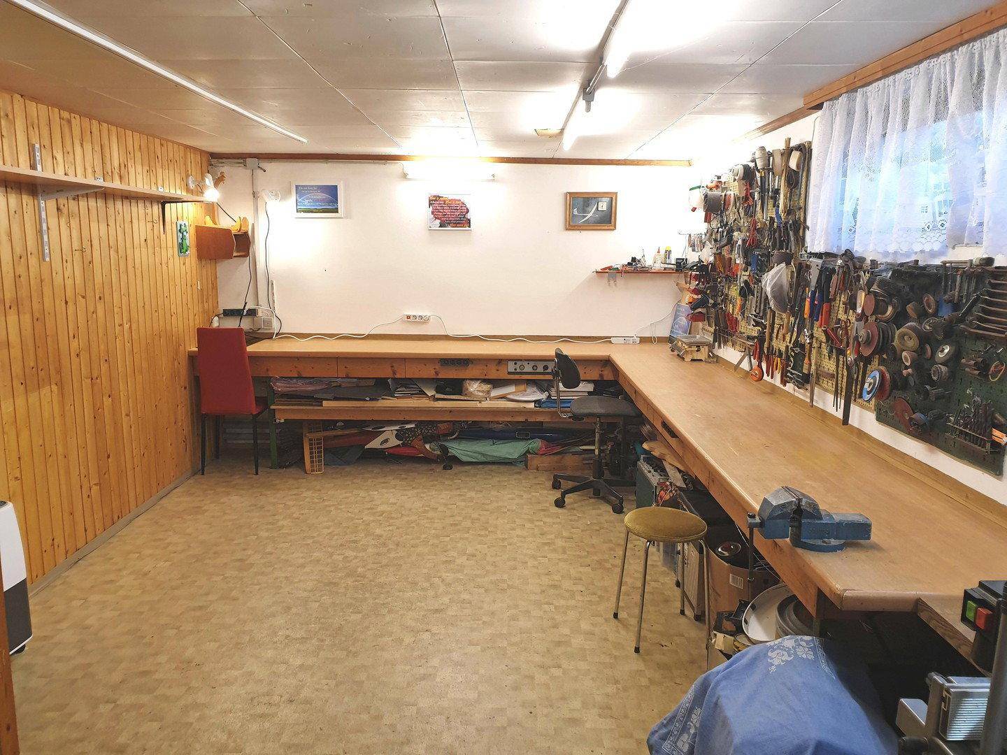 Geräumiger Hobbyraum im Keller mit langen Werkbänken und vielen Werkzeugen an der Wand.