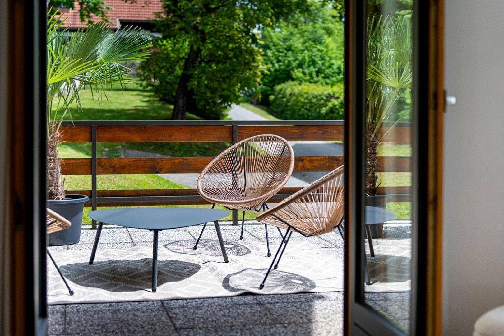 Gemütlicher Sitzbereich auf dem Balkon mit Korbstühlen, Tisch und Blick ins Grüne.