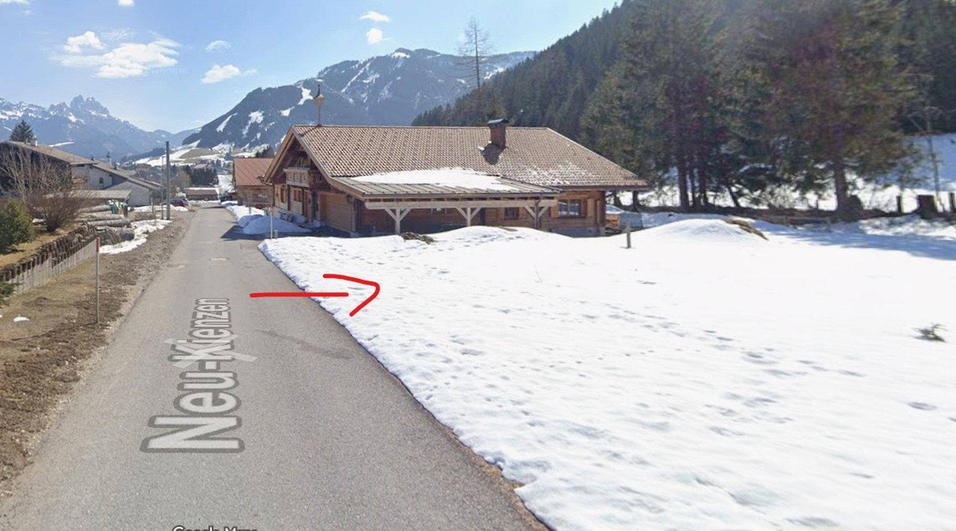 Schneebedeckte Straße mit einem Haus im alpenländischen Stil und einem weiten Bergpanorama.