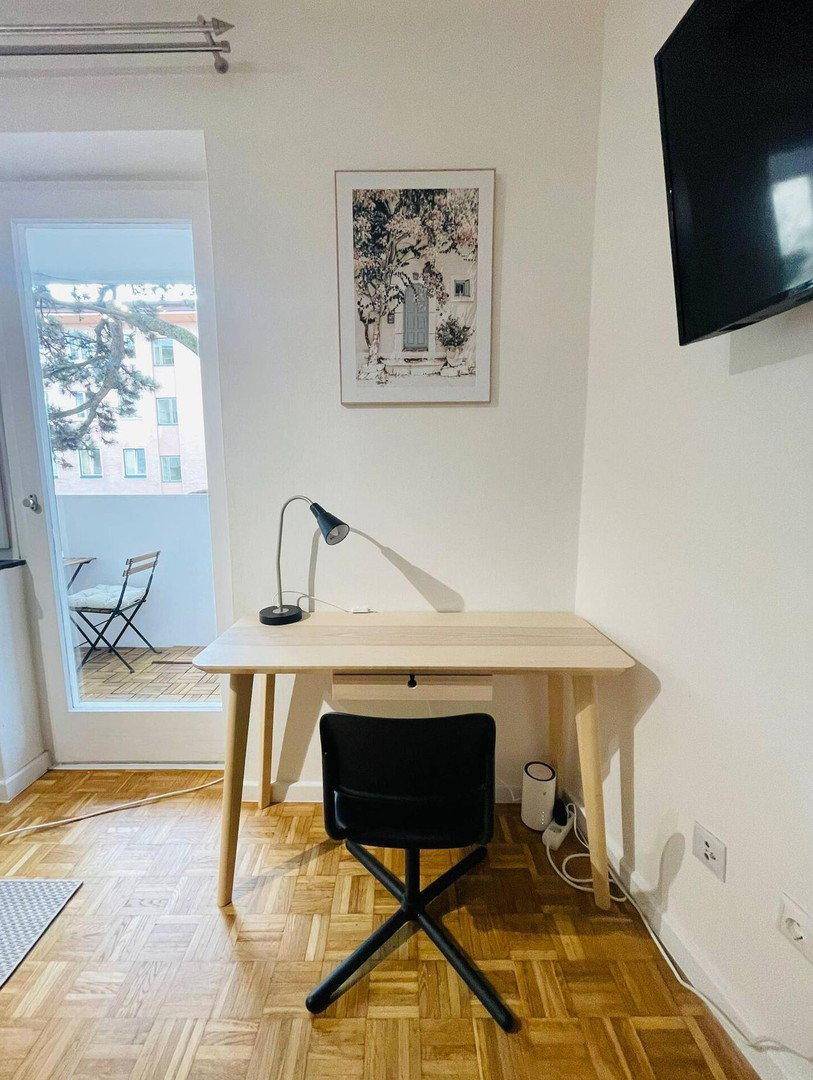 Arbeitsbereich mit Schreibtisch, Stuhl und Lampe, direkt neben dem Balkonzugang.