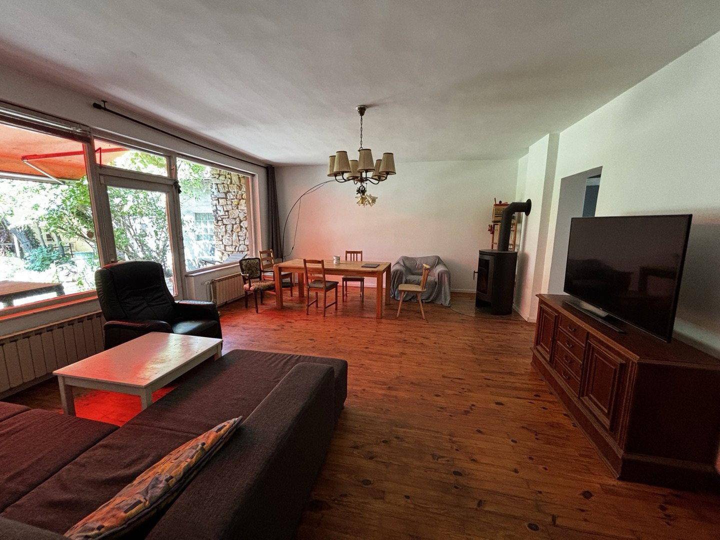 Geräumiger Wohnbereich mit Holzboden, Kaminofen und großen Fenstern zum Außenbereich.