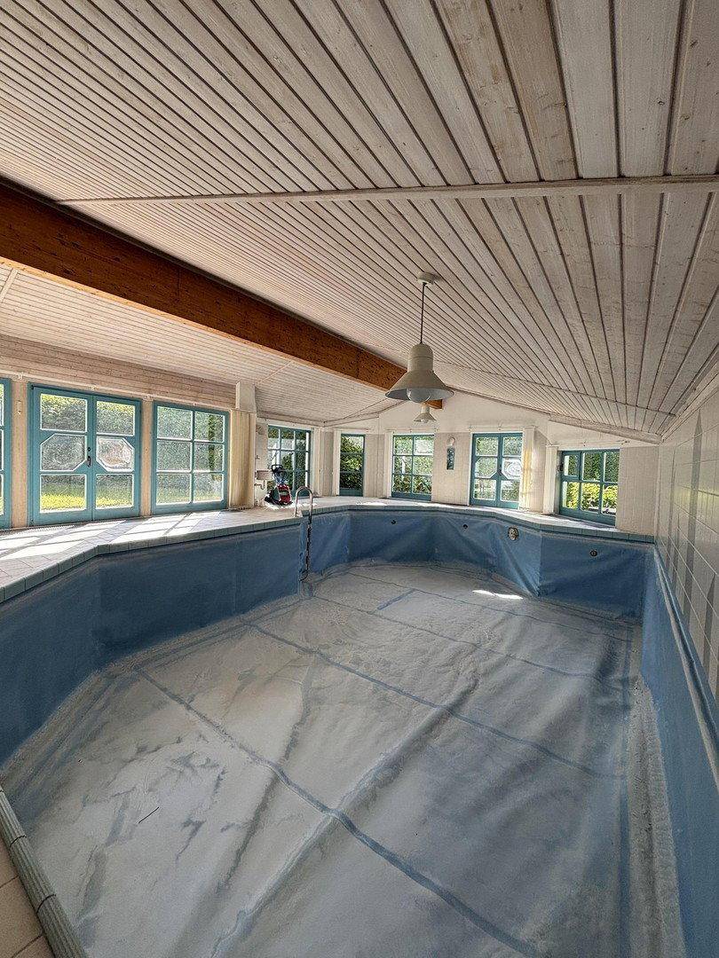 Großer Innenpoolbereich mit Holzdecke, vielen Fenstern und Blick in den Garten.