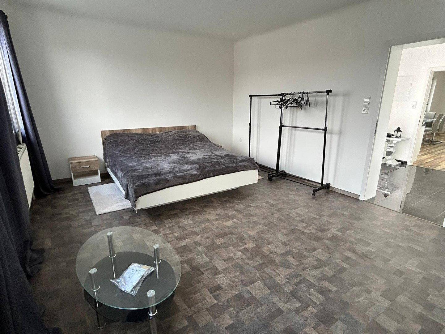 Schlafzimmer mit Doppelbett, Couchtisch und Kleiderstange, Zugang zum Flur.