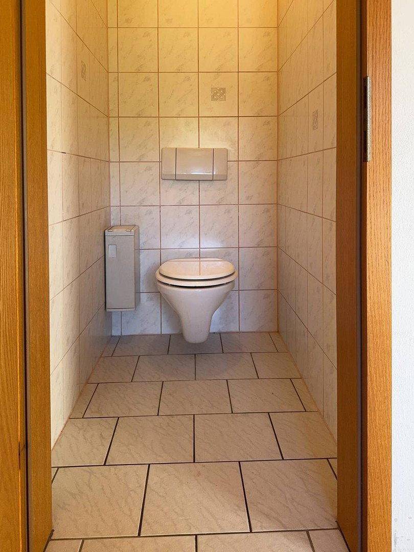 Separate Toilette mit Wand-WC und hellen Fliesen an Wänden und Boden.