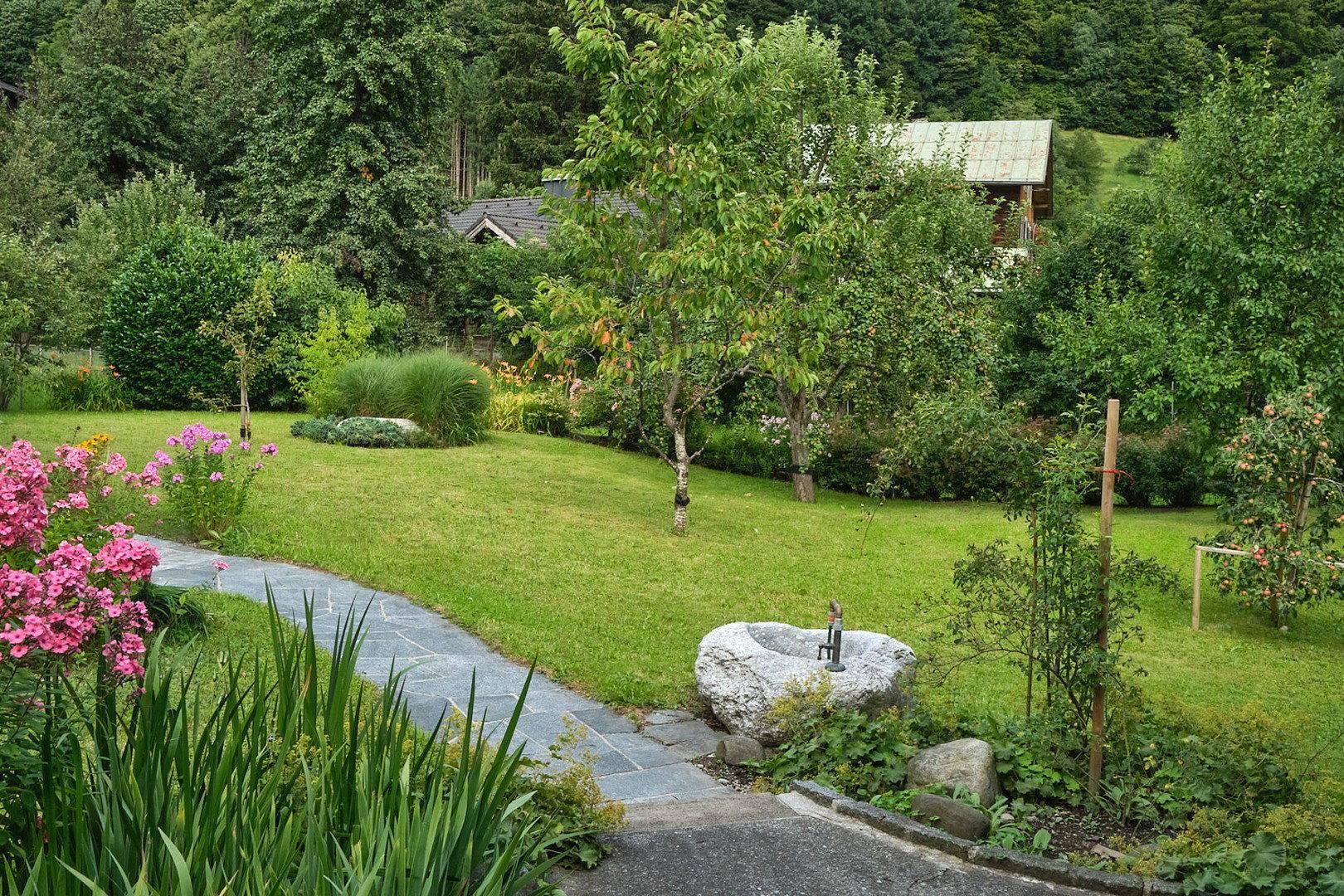 Idyllischer Gartenweg aus Steinplatten, umgeben von üppigem Grün und blühenden Pflanzen.