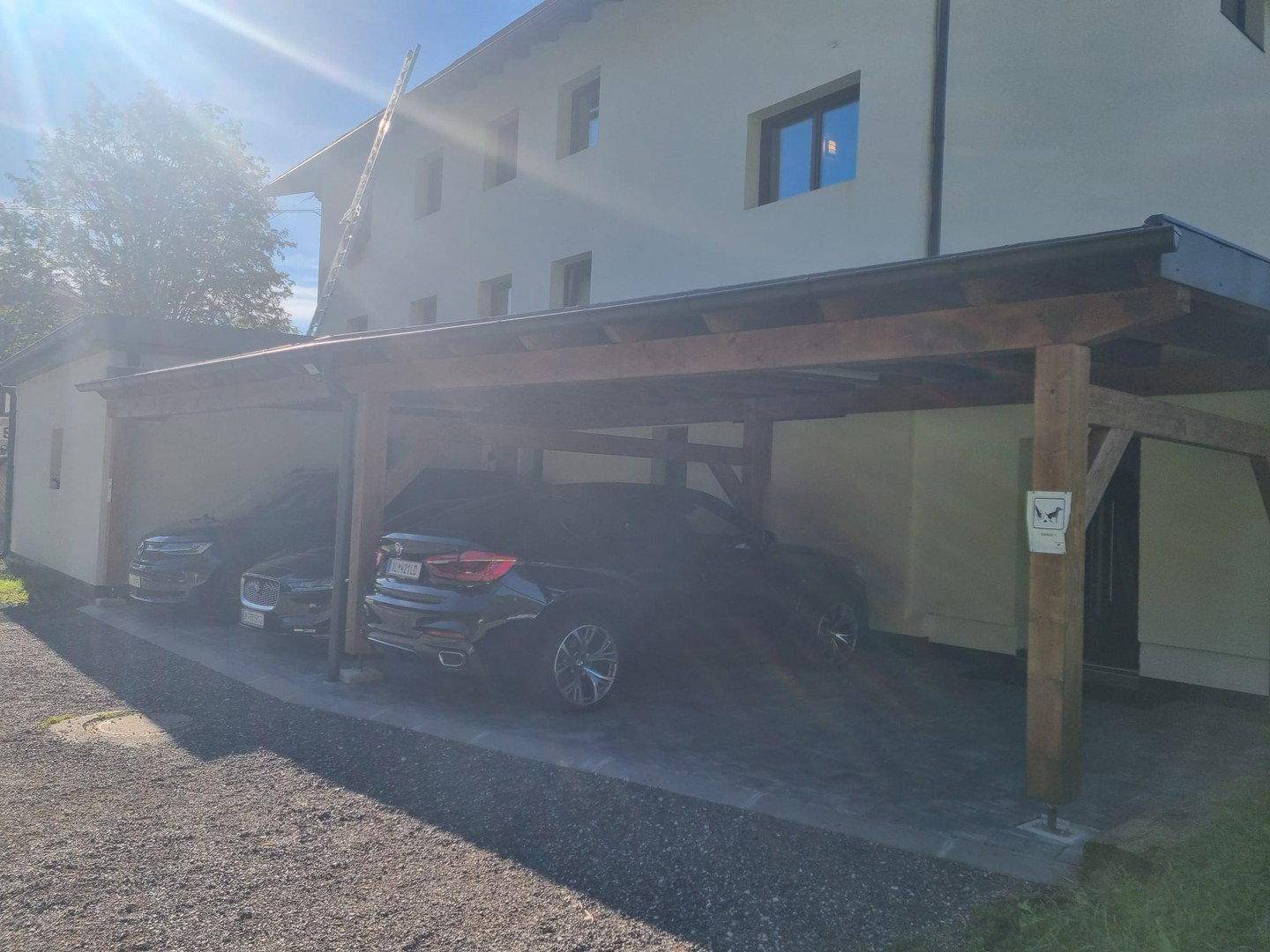 Holzcarport mit mehreren geparkten Autos vor einem Wohngebäude.