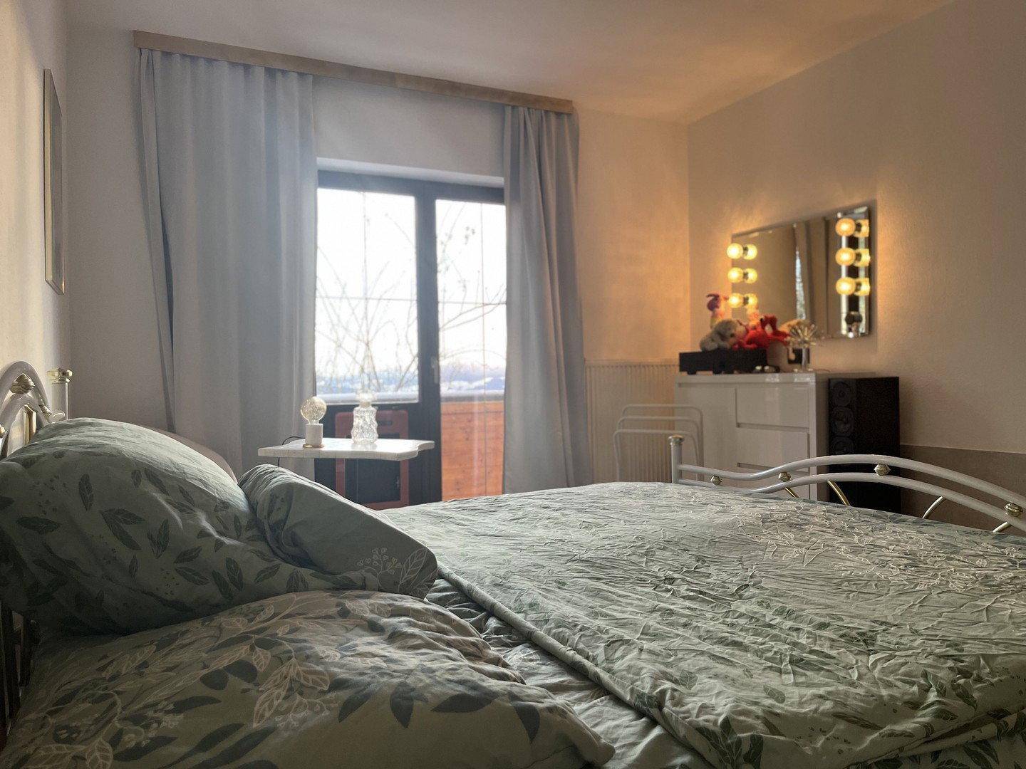 Schlafzimmer mit Doppelbett, Schminktisch und Balkonzugang mit Blick auf die verschneite Landschaft.