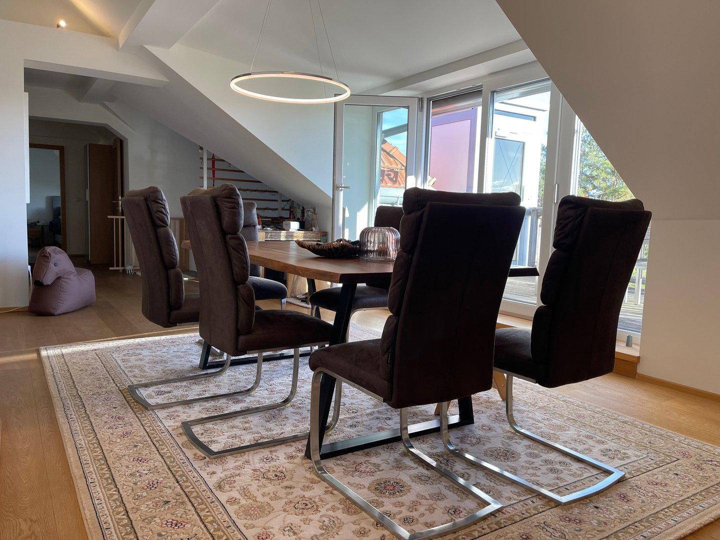 Eleganter Essbereich mit Holztisch und modernen Freischwinger-Stühlen auf einem gemusterten Teppich.