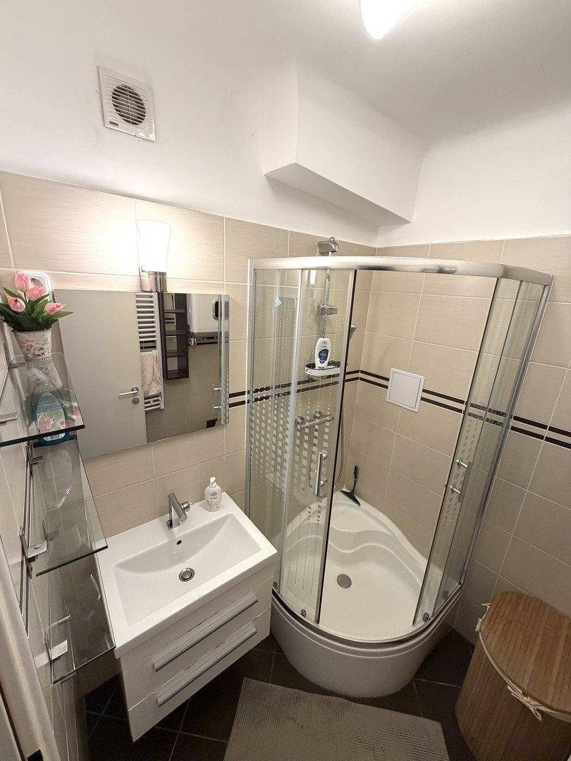 Modernes Badezimmer mit Eckdusche, Waschbecken und hellen Fliesen, gut beleuchtet.