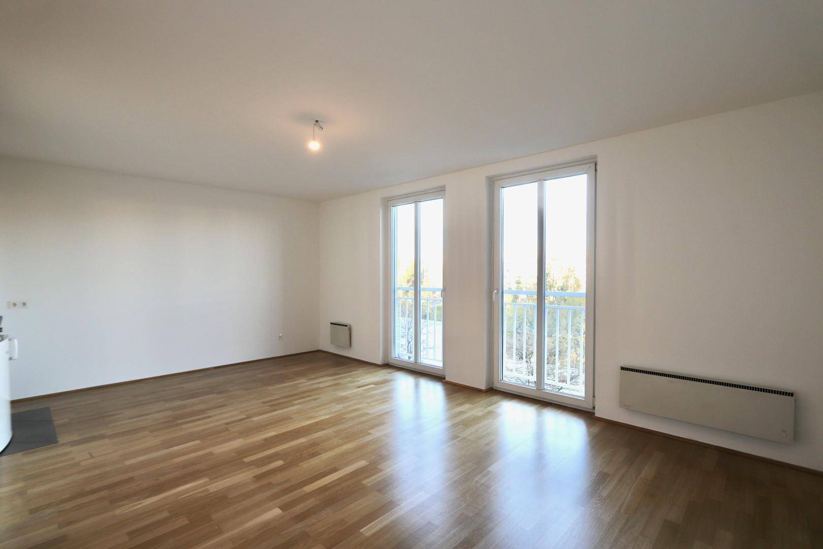Geräumiges Wohnzimmer mit hellem Parkettboden und zwei großen Fenstern, die viel Licht hereinlassen.