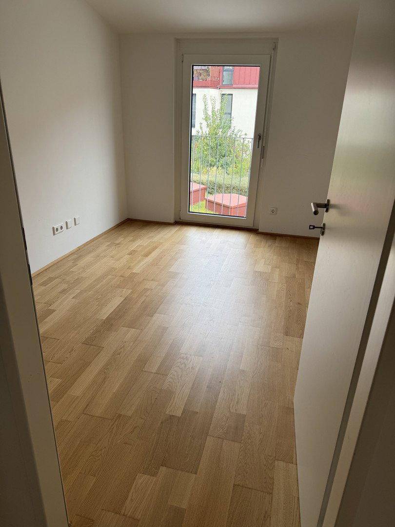 Helles Schlafzimmer mit Holzfußboden und französischem Balkon, der eine angenehme Wohnatmosphäre schafft.