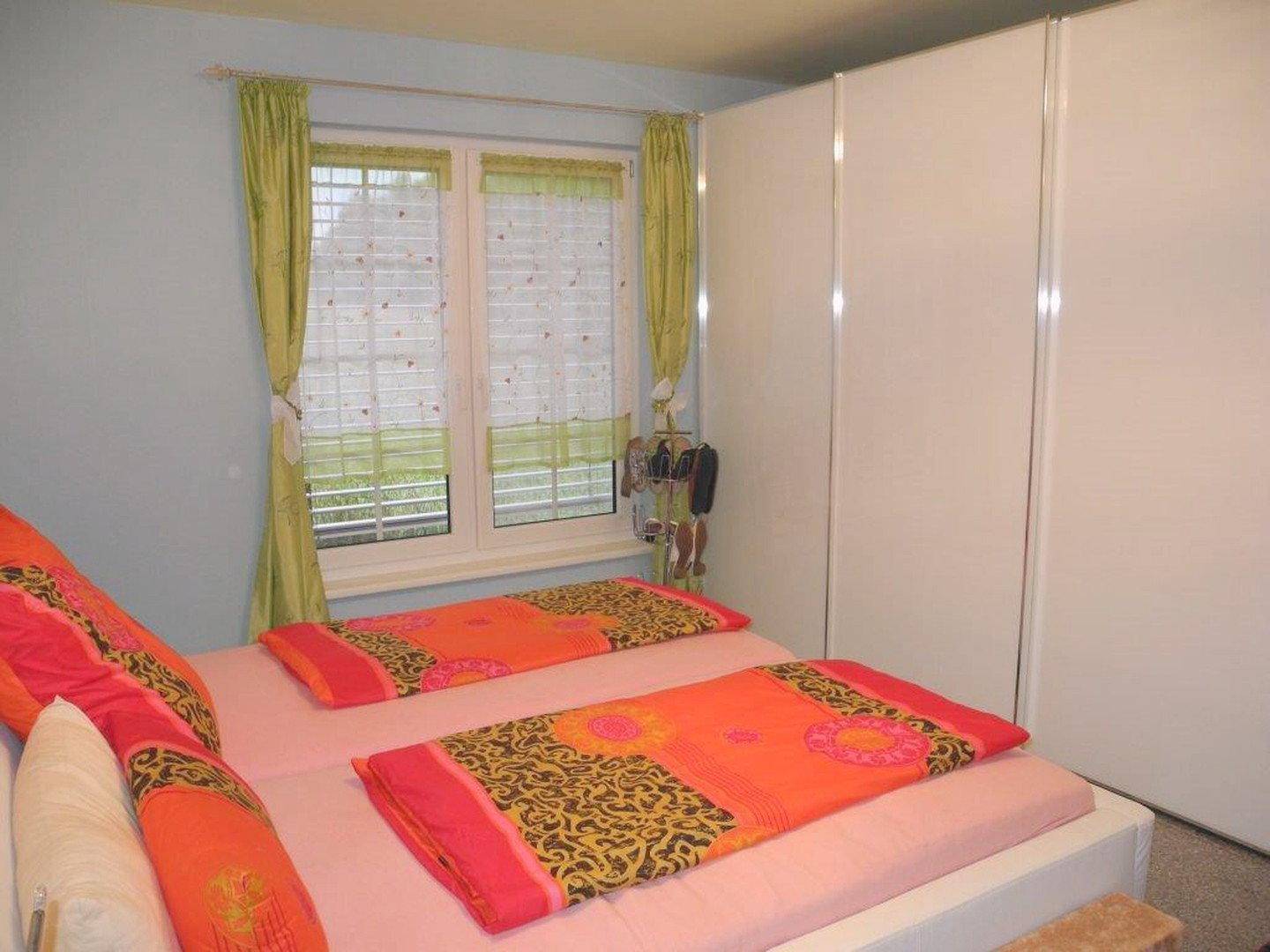 Schlafzimmer mit Doppelbett, weißen Einbauschränken und Fenster mit Blick ins Grüne.