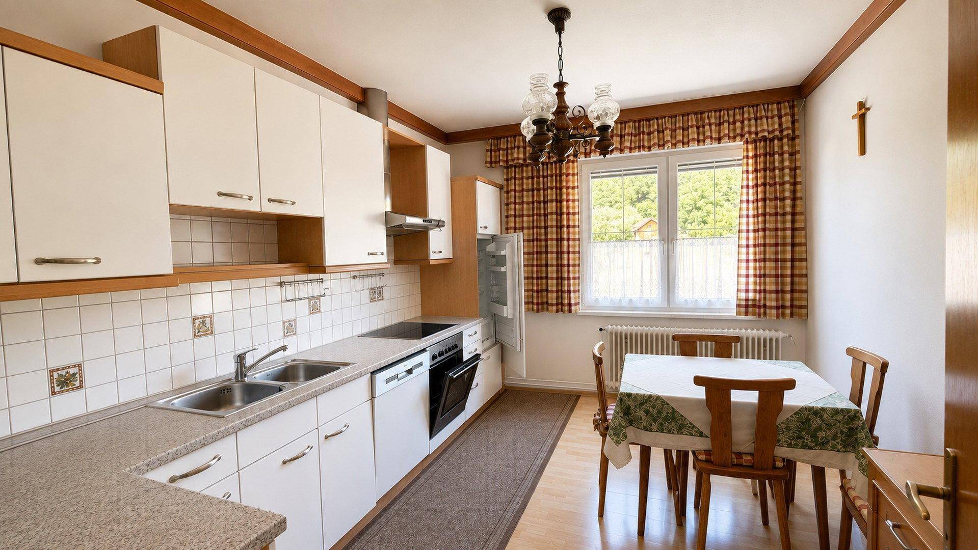 Traditionelle Küche mit weißen Schränken, Fliesenrückwand und Essbereich am Fenster.