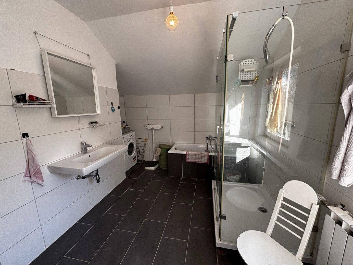 Modernes Badezimmer mit dunklen Fliesen, Dusche und Badewanne unter der Dachschräge.