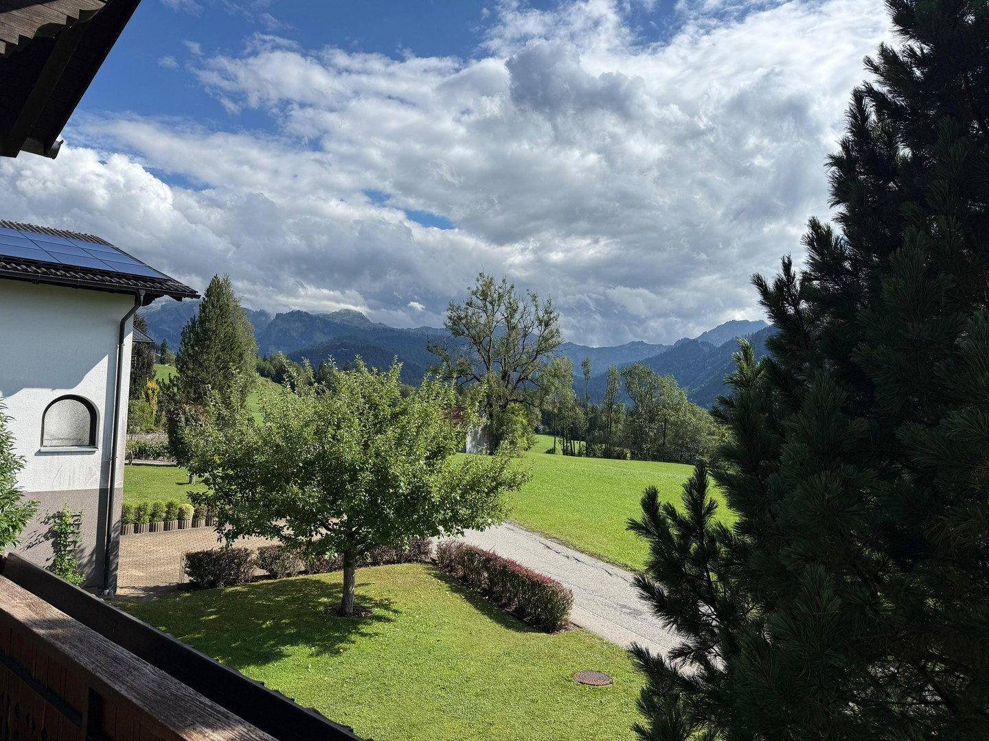 Malerischer Ausblick auf grüne Wiesen und majestätische Berge unter bewölktem Himmel.