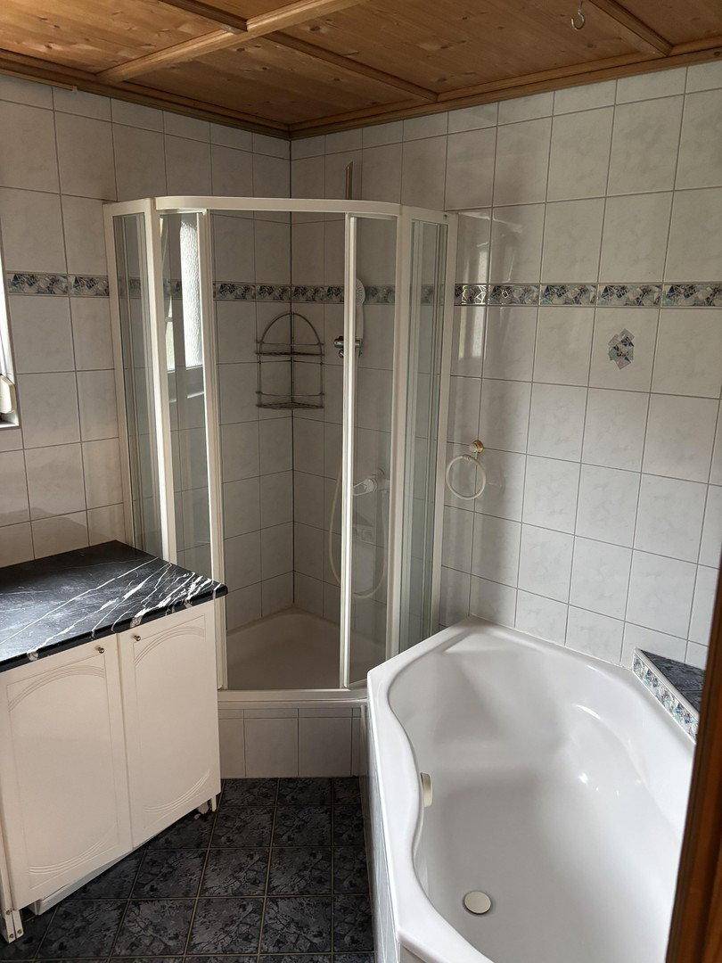 Badezimmer mit Eckbadewanne, Duschkabine, gefliesten Wänden und Decke aus Holz.