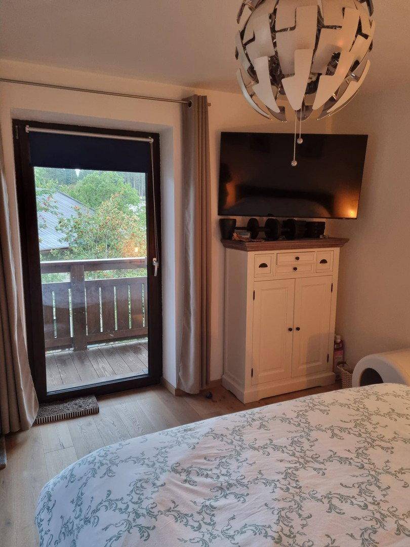 Schlafzimmer mit Balkonzugang, Fernseher und Holzboden, bietet Blick ins Grüne.