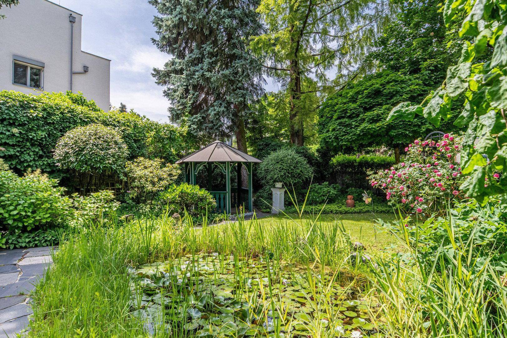 Idyllischer Garten mit Seerosen-Teich, üppiger Bepflanzung und einem Pavillon.