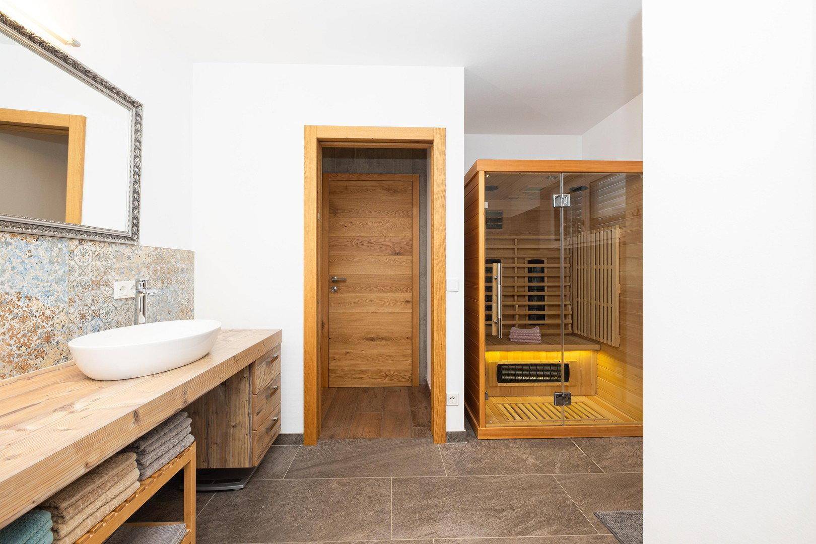 Badezimmer mit Holzwaschtisch, Spiegel und einer modernen Infrarot-Saunakabine.