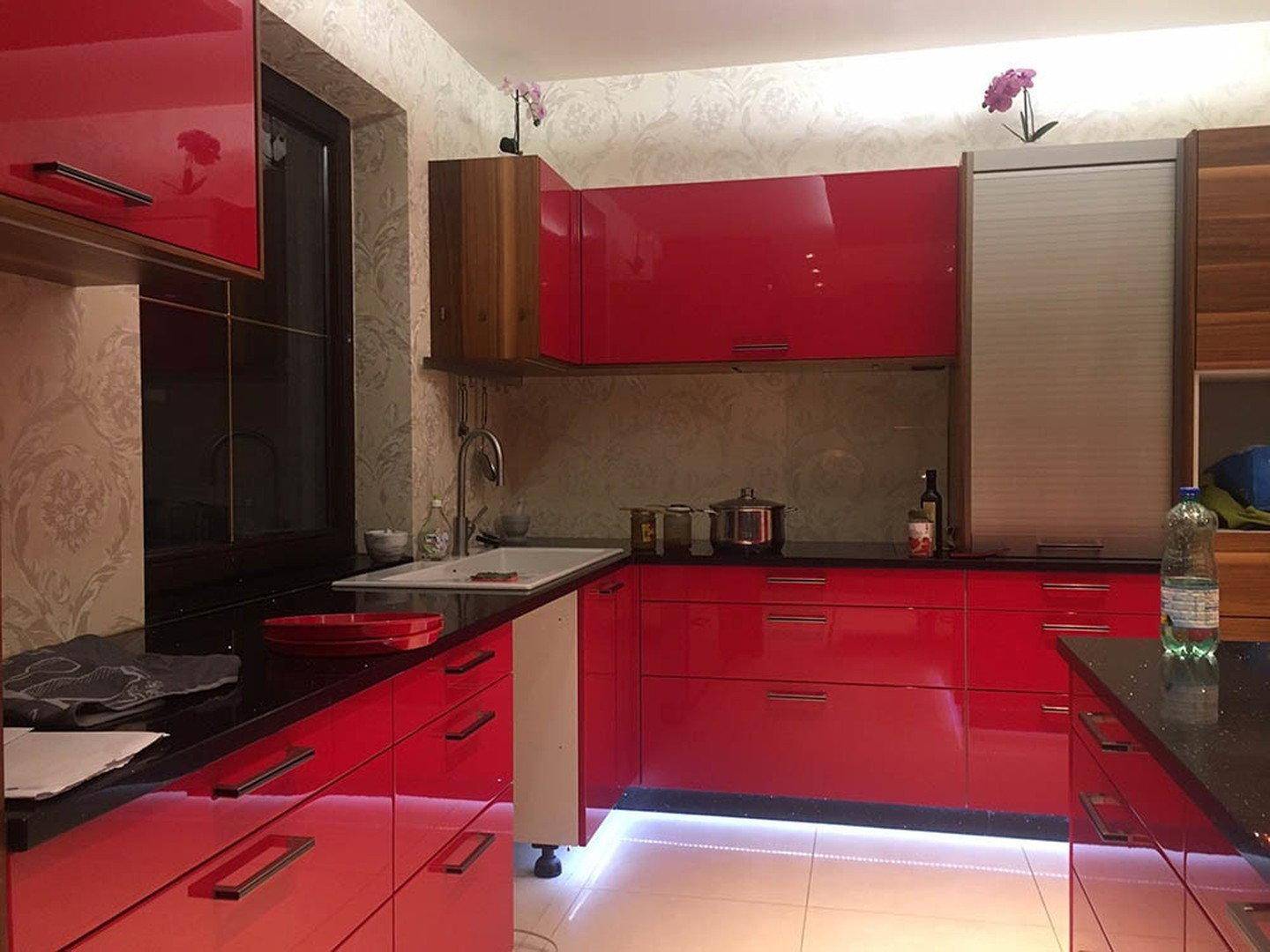 Moderne Küche mit leuchtend roten Hochglanzschränken, schwarzen Arbeitsplatten und integrierter Spüle.