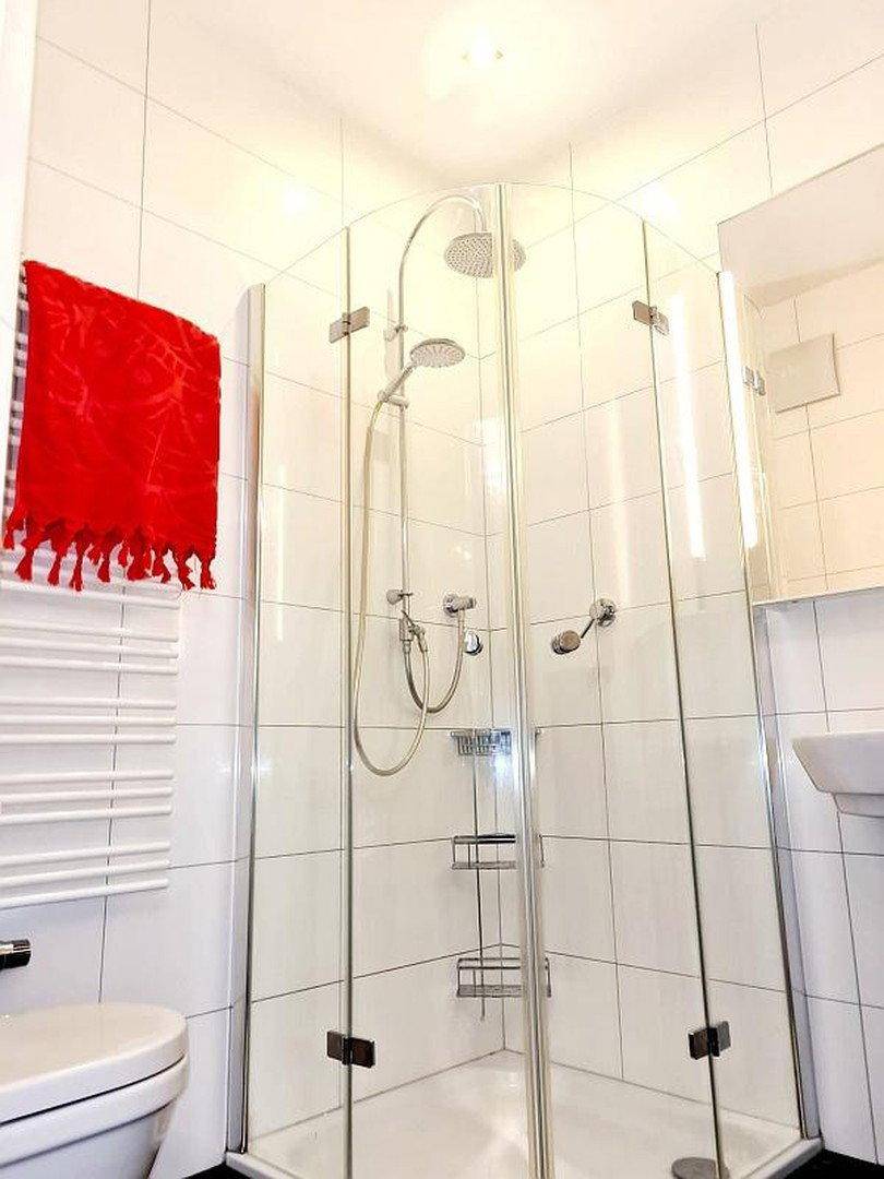 Modernes Badezimmer mit Eckdusche, weißen Fliesen und beheiztem Handtuchhalter.