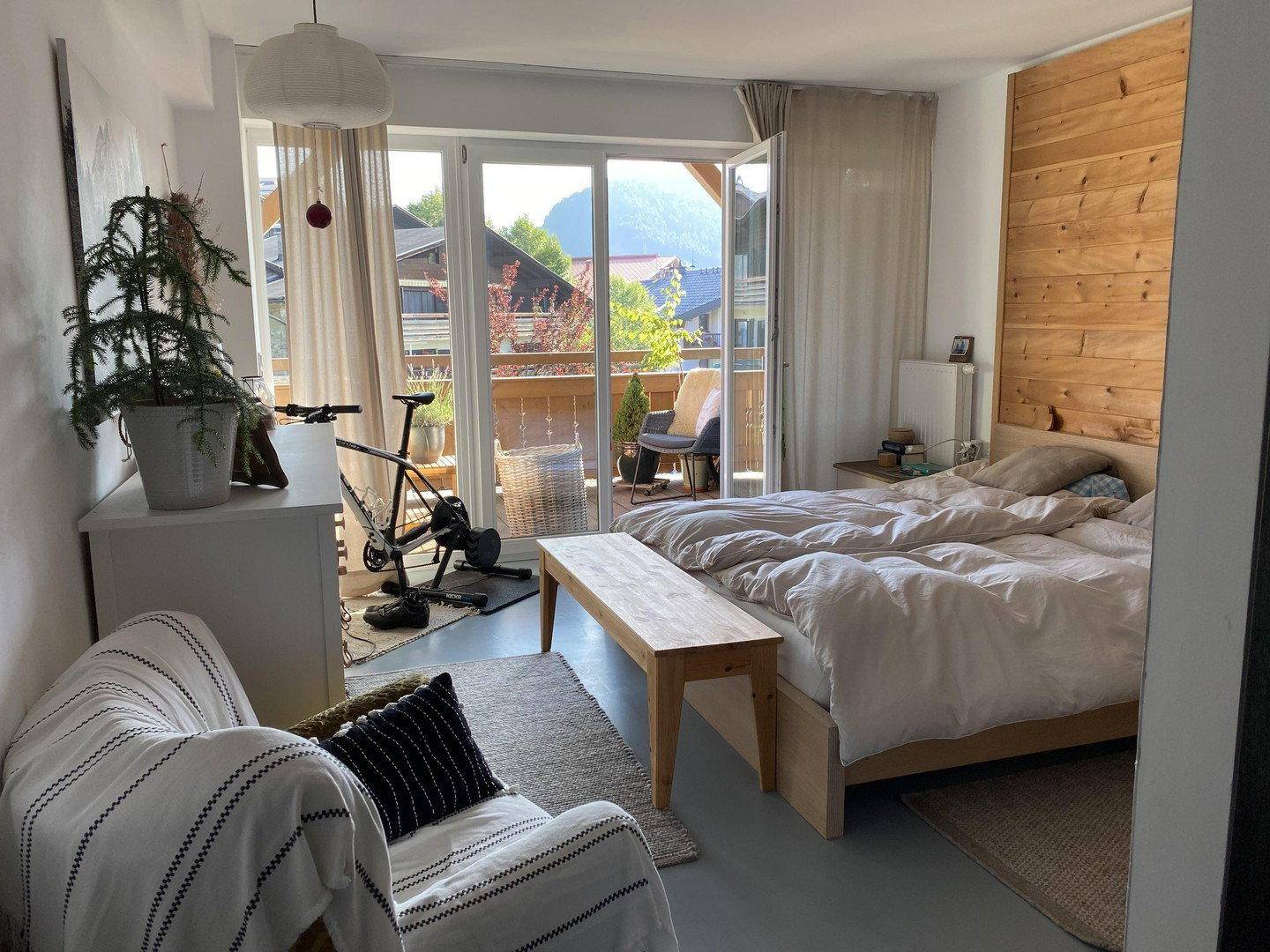 Helles Schlafzimmer mit Doppelbett, Holzwand und Zugang zum Balkon.