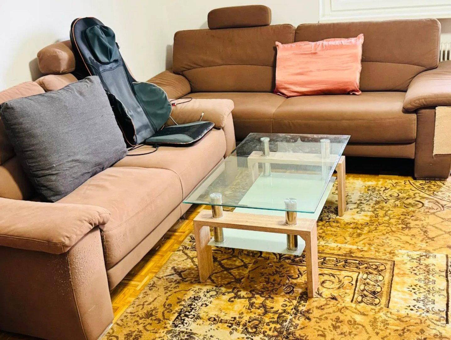 Gemütliches Wohnzimmer mit zwei braunen Sofas, einem Glastisch und einem gemusterten Teppich.